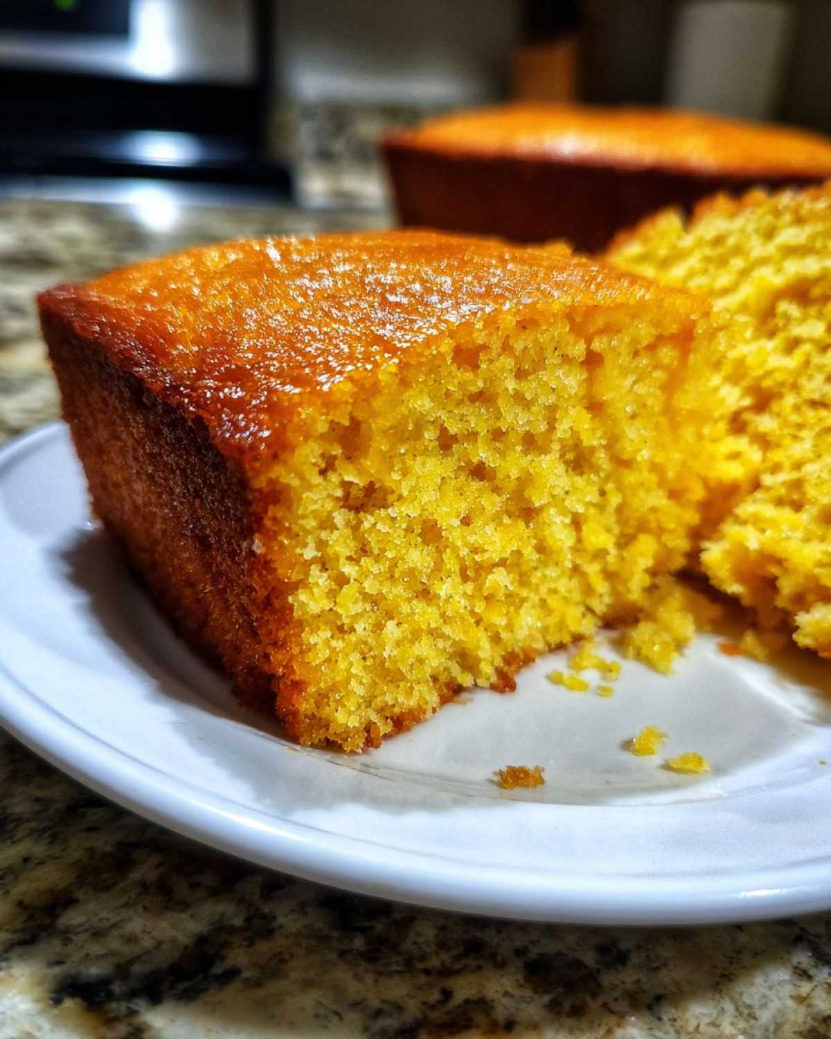 Close-up of a moist, golden slice of sourdough cornbread with a shiny top, served on a white plate.