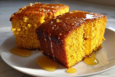 Two moist slices of bright orange sweet potato cornbread drizzled generously with a shiny amber glaze.
