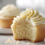 Close-up of a vanilla cupcakes with a bite taken out, showing the moist crumb and swirl of vanilla frosting.
