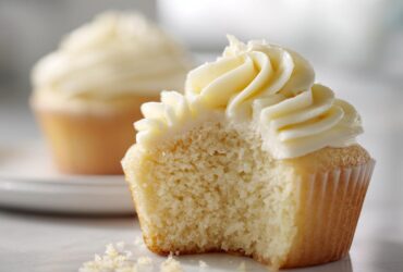 Close-up of a vanilla cupcakes with a bite taken out, showing the moist crumb and swirl of vanilla frosting.