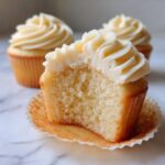 Close-up of a vanilla cupcake cut in half showing the moist crumb and creamy frosting of the amazing vanilla cupcakes.