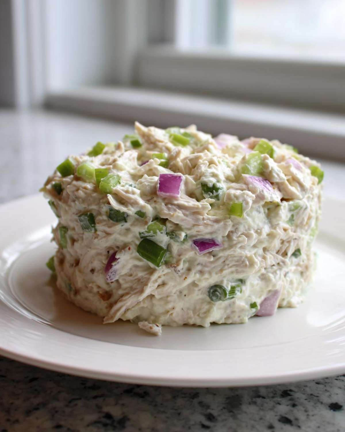 A perfectly molded serving of creamy cottage cheese chicken salad topped with diced green onions and red onion.
