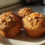 Three golden brown morning glory muffins topped with chopped nuts and visible shreds of carrot.