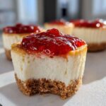 A close-up of a no-bake cheesecake bites cut in half showing the graham cracker crust, creamy filling, and strawberry topping.