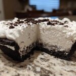 Close-up of a slice missing from a no-bake ice cream pie showing thick white filling and dark crust.