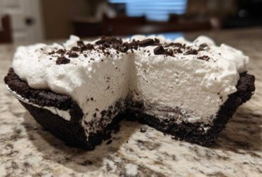 Close-up of a slice missing from a no-bake ice cream pie showing thick white filling and dark crust.