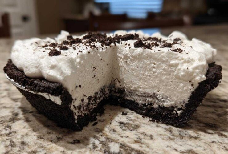 Close-up of a slice missing from a no-bake ice cream pie showing thick white filling and dark crust.