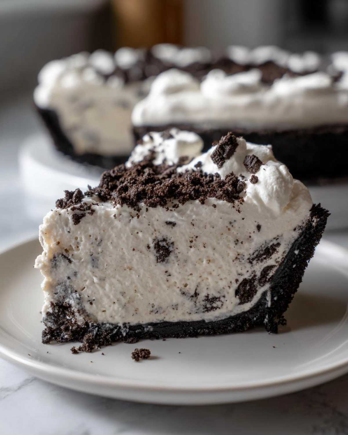 A close-up slice of no-bake ice cream pie with a dark chocolate crust, creamy filling, and cookie crumbles on top.