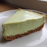 A close-up of a creamy, pale green slice of no-bake key lime cheesecake with a thick graham cracker crust.