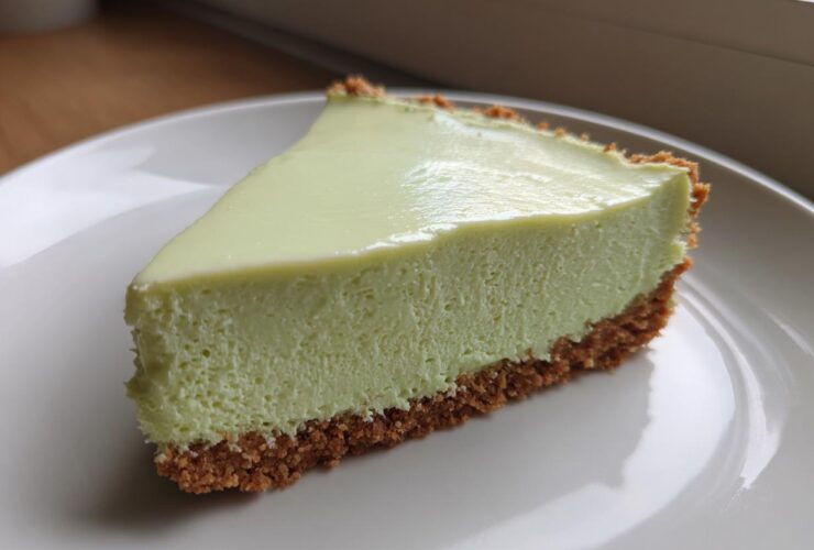 A close-up of a creamy, pale green slice of no-bake key lime cheesecake with a thick graham cracker crust.