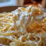 Close-up of fettuccine pasta generously coated in creamy Olive Garden Alfredo Sauce being lifted by a fork.