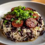 Close-up of a serving of black beans and rice topped with sliced sausage and fresh parsley.