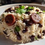 Close-up of a molded serving of seasoned black beans and rice mixed with slices of sausage and garnished with cilantro.