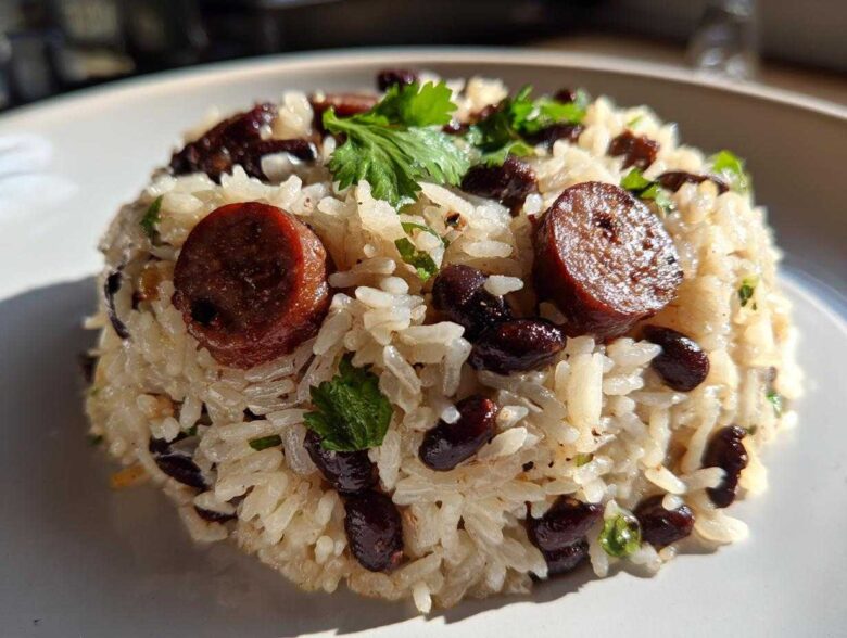 Close-up of a molded serving of seasoned black beans and rice mixed with slices of sausage and garnished with cilantro.