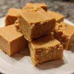 Close-up of several squares of creamy, light brown penuche fudge stacked on a white plate.