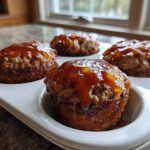 Four perfectly baked mini meatloaf portions topped with a shiny, amber glaze, resting in a white muffin tin.