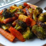 A white plate piled high with perfectly roasted vegetables, featuring charred broccoli florets and bright orange carrots.