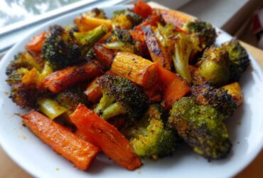 A white plate piled high with perfectly roasted vegetables, featuring charred broccoli florets and bright orange carrots.