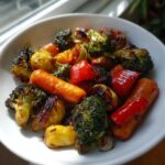 Close-up of perfectly roasted vegetables including charred broccoli, carrots, and red peppers in a white bowl.
