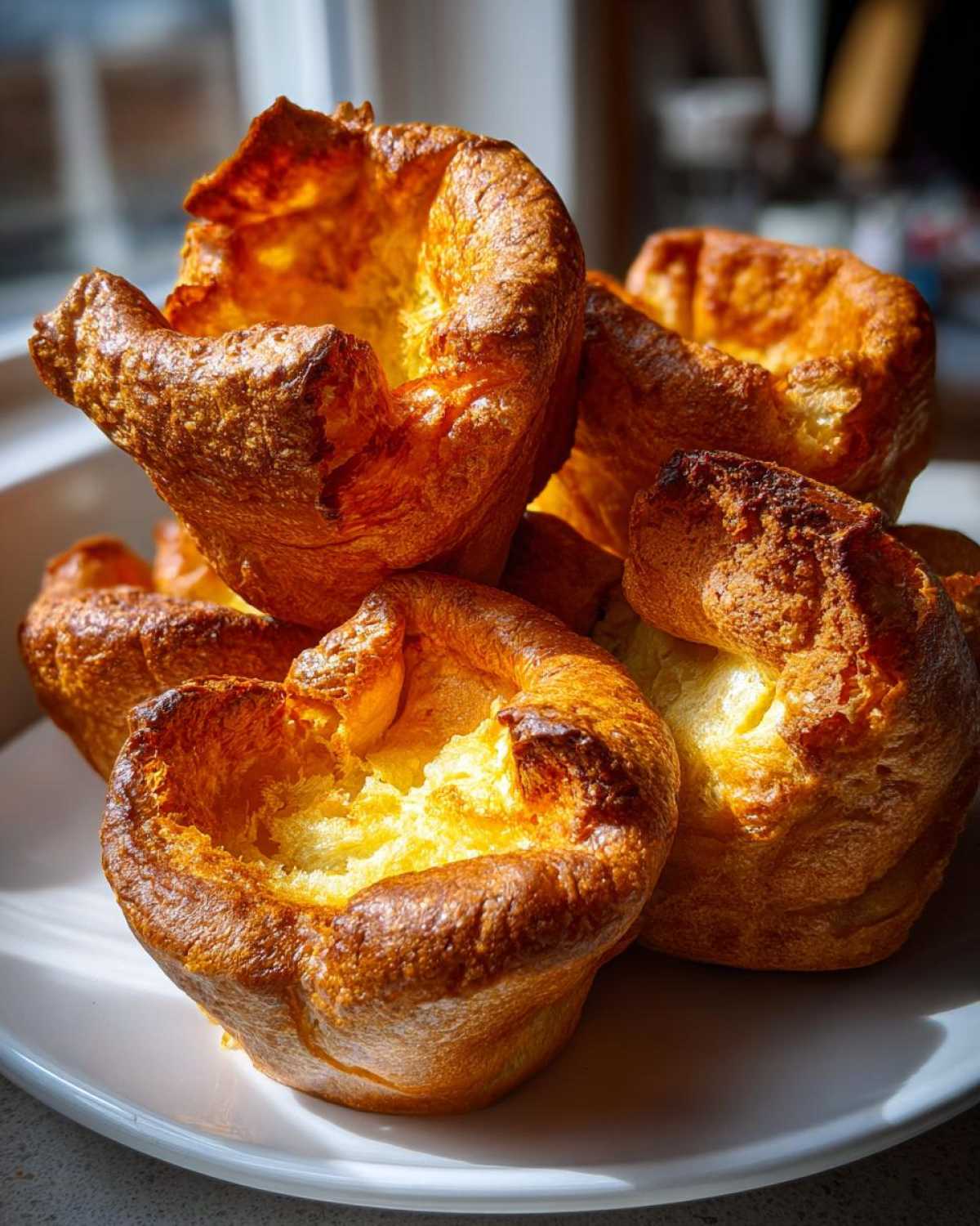 A close-up of several golden brown, perfectly risen yorkshire pudding piled high on a white plate.