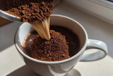 Close-up of homemade hot cocoa mix powder being poured into a white mug containing liquid.