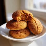 A stack of four soft pumpkin snickerdoodle cookies, one broken open to show the texture.