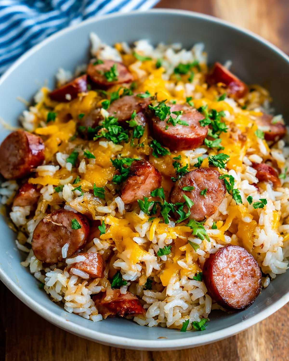 A close-up of a bowl filled with sausage and rice, topped with melted cheddar cheese and fresh parsley.