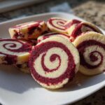 Close-up of several red velvet pinwheel cookies showing distinct red and white swirls on a white plate.