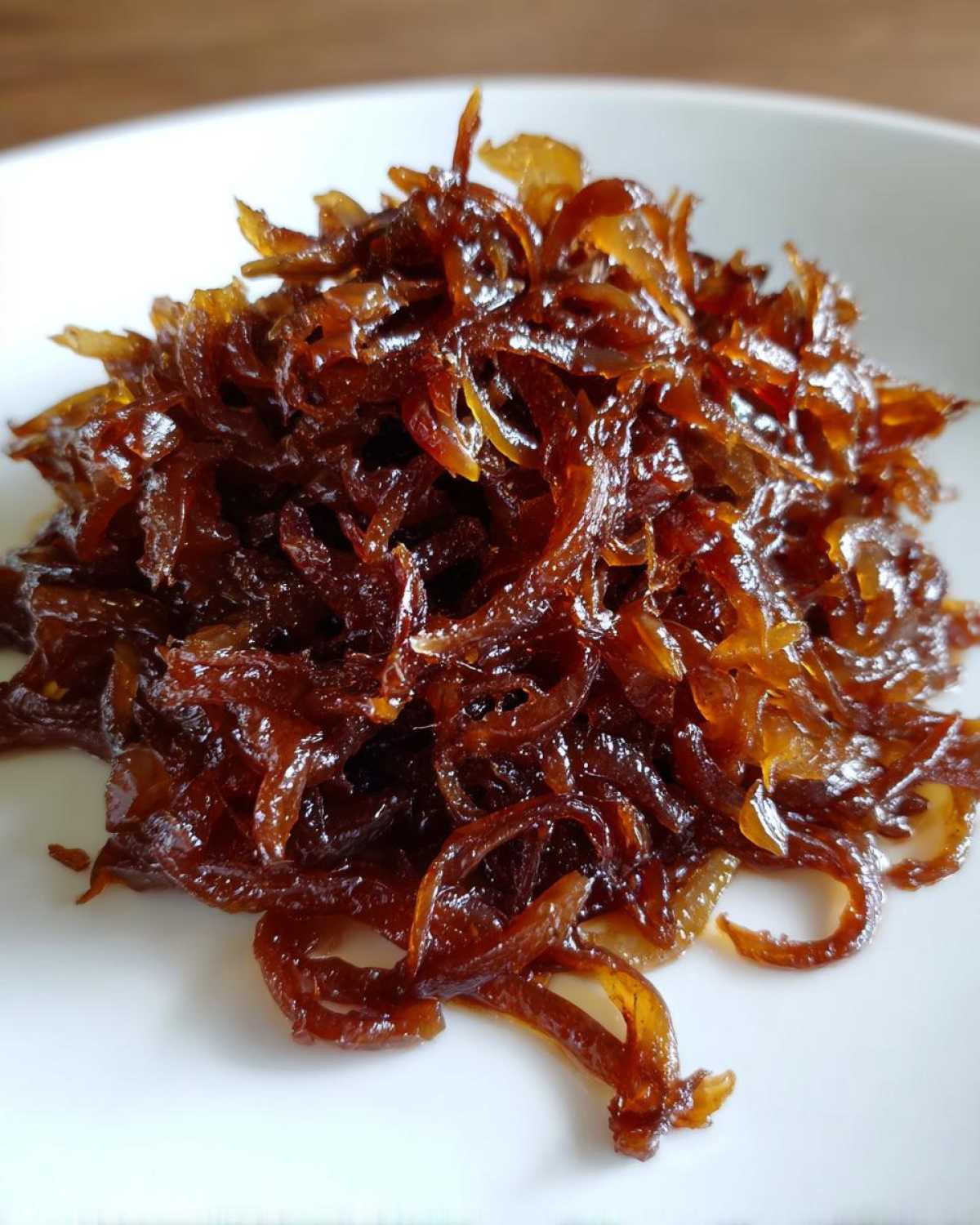 A close-up of a mound of deeply brown, glossy caramelized onions served on a white plate.
