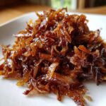 A close-up of a mound of deeply browned, glossy caramelized onions served on a white plate.
