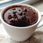 Close-up of a freshly baked, rich chocolate mug cake topped with chocolate chips.