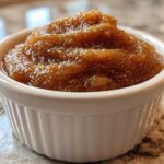 A close-up of thick, rich brown pear butter served in a small white fluted ramekin.
