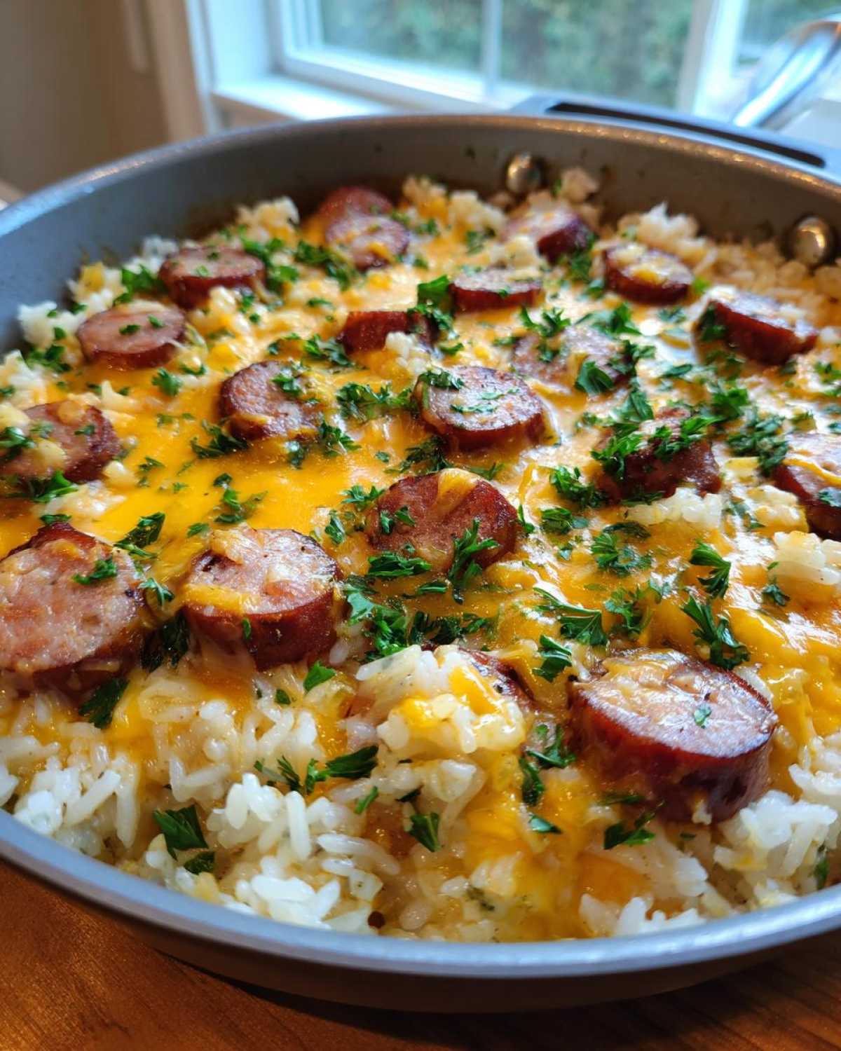 Close-up of a skillet filled with cheesy sausage and rice, topped with melted cheddar and fresh parsley.