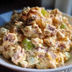 A close-up, bright photo of a creamy ham salad recipe served in a white bowl, topped with paprika.