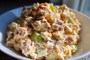 A close-up, bright photo of a creamy ham salad recipe served in a white bowl, topped with paprika.