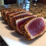 Five thick slices of perfectly seared ahi tuna, crusted with pepper, showing a rare, deep red center.
