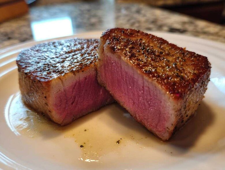 Two thick slices of perfectly seared tuna steak, showing a bright pink, medium-rare interior, seasoned with pepper.