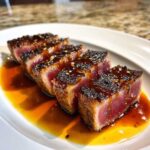 Four thick slices of perfectly seared tuna steak, rare in the center, drizzled with a dark glaze and sesame seeds.
