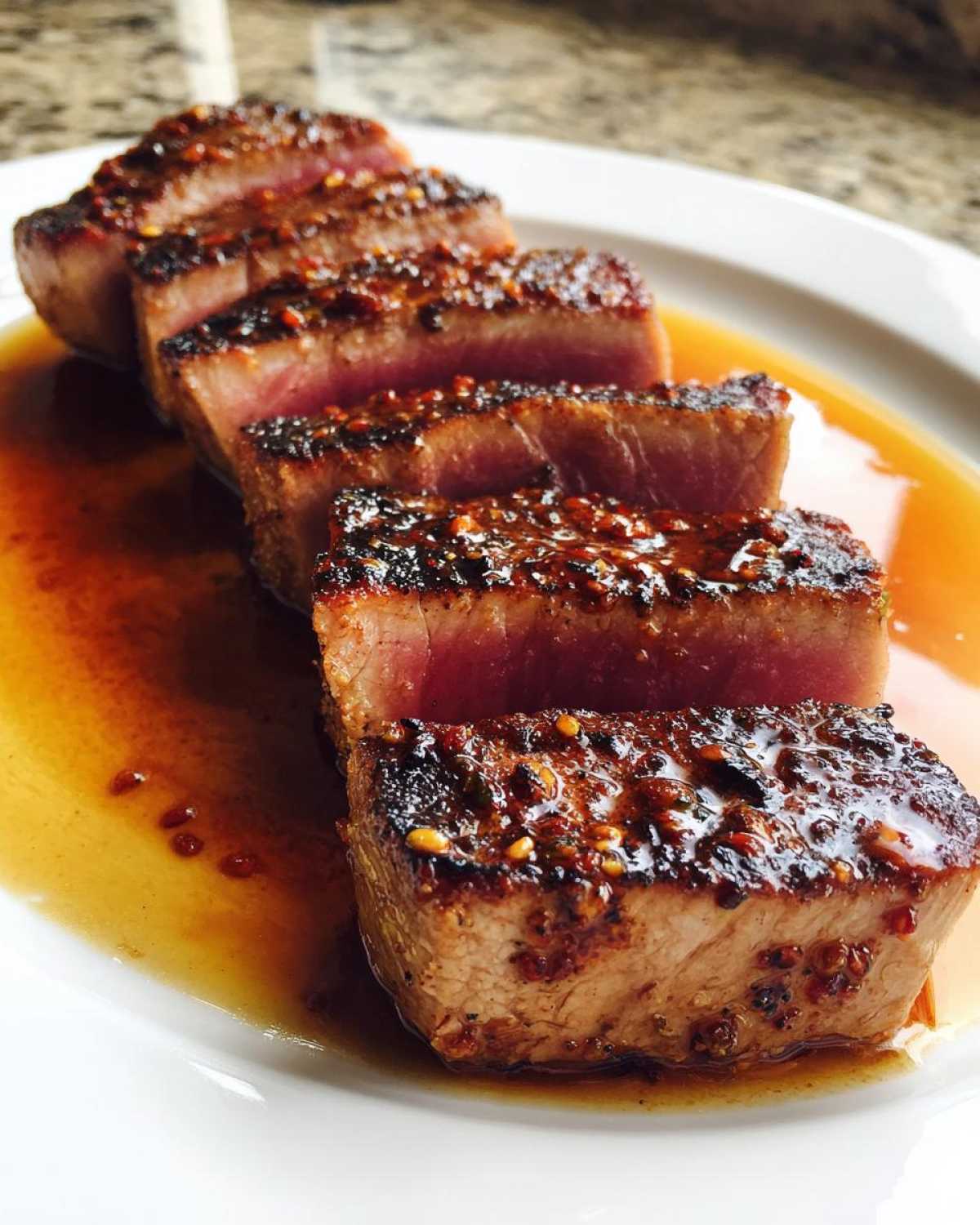 Close-up of five slices of perfectly seared Tuna Steak, rare in the center, sitting in a savory glaze.