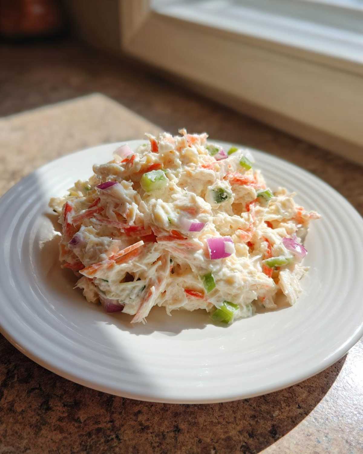 A mound of creamy crab salad mixed with shredded carrots, red onion, and celery on a white plate.