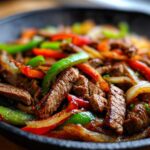Close-up of sizzling steak fajitas with colorful bell peppers and onions served in a black cast iron skillet.