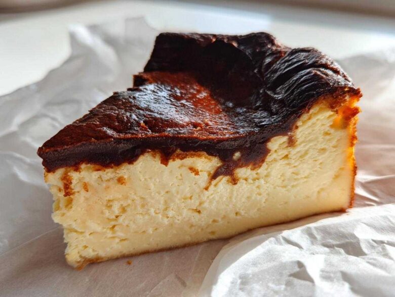 A close-up slice of creamy Basque cheesecake showing its signature dark, caramelized top.