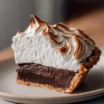 Close-up of a thick slice of chocolate meringue pie showing rich filling and perfectly torched meringue.