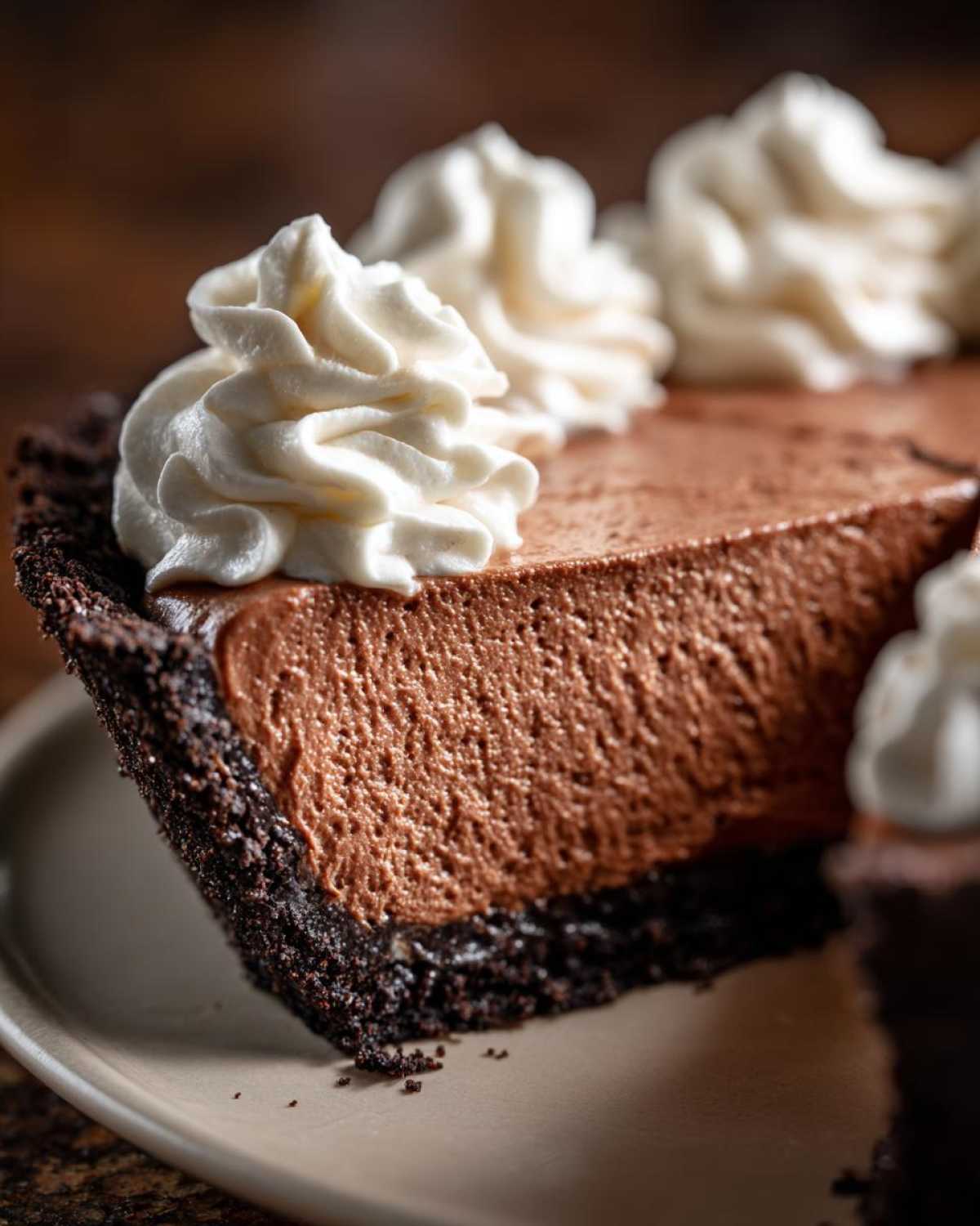 Close-up of a thick slice of chocolate mousse pie showing the airy filling and dark crust, topped with swirls of whipped cream.