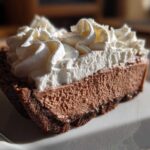 Close-up of a rich slice of chocolate mousse pie with a dark crust and generous topping of white whipped cream.