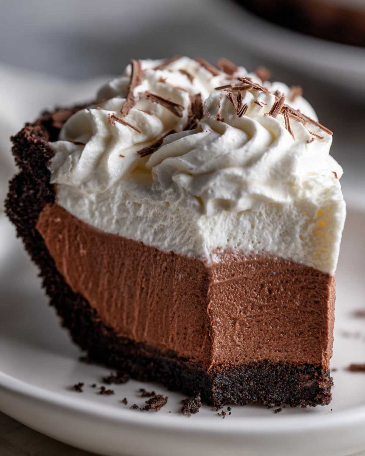 Close-up of a perfect slice of chocolate mousse pie showing a dark crust, thick chocolate filling, and whipped cream topping.