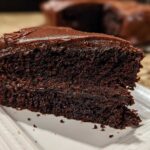 Close-up of a rich, dark slice of homemade chocolate cake topped with glossy chocolate frosting.