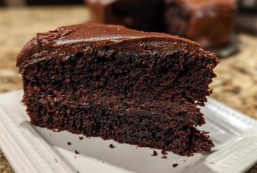 Close-up of a rich, dark slice of homemade chocolate cake topped with glossy chocolate frosting.