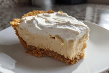 A thick slice of creamy peanut butter pie with a graham cracker crust and a generous topping of whipped cream.