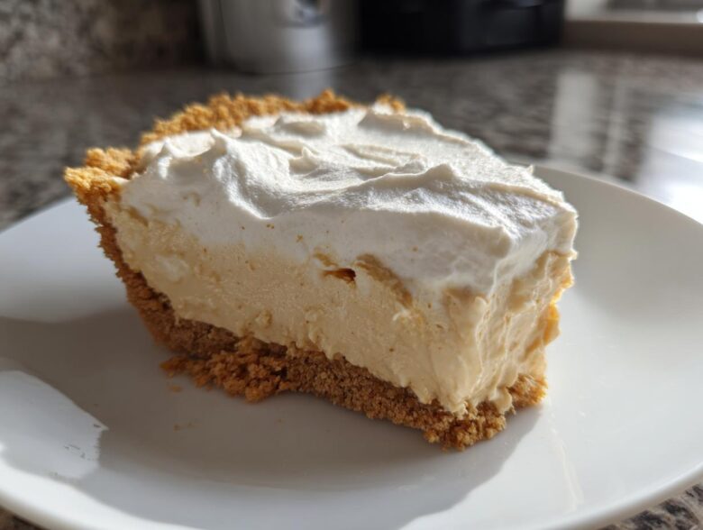 A thick slice of creamy peanut butter pie with a graham cracker crust and a generous topping of whipped cream.